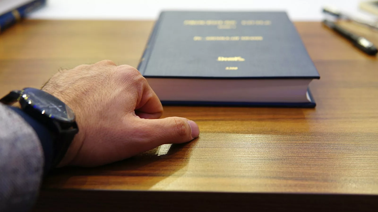 Persona sostenint llibre cobert negre sobre taula de fusta marró
